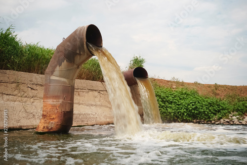 Wastewater from two large rusty pipes merge into the river in clouds of steam