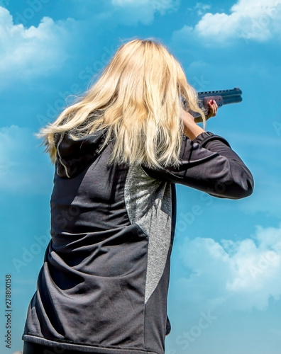 Young girl with blond hair with a weapon for shooting at flying targets against the sky with clouds