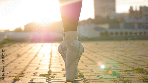 Legs of young woman ballerina standing on the roof on her tiptoes - sunset