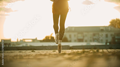 Legs of graceful young woman ballerina running on the roof on her tiptoes - sunset