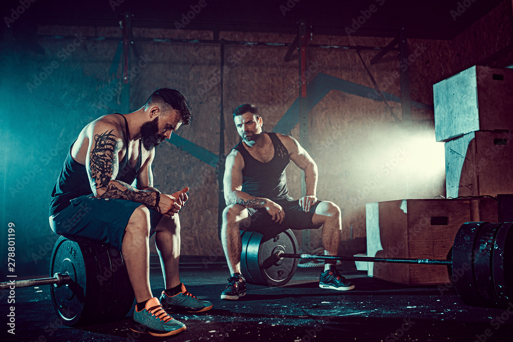 Two muscular bearded tattoed athletes relax after training, lifting heavy weight. smoke at gym. Scream. Working hard. Exercise for the muscles of the back Two muscular bearded tattoed athletes relax after training, lifting heavy weight. smoke at gym. Scream. Working hard. Exercise for the muscles of the back