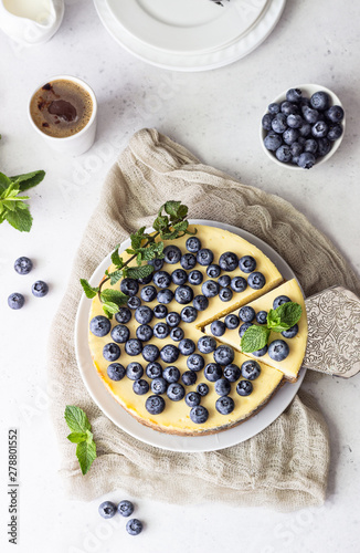 New York style cheesecake, fresh blueberries and mint on a white plate. Light stone background. Copy space.