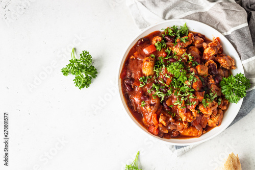 Meat stew with red beans, bell pepper and onion in tomato sauce in a white plate over light grey slate or stone background. 