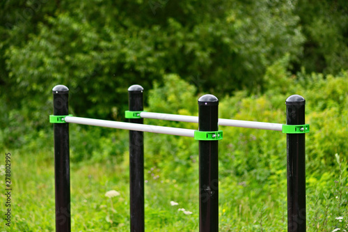 Stationary parallel horizontal bars for outdoor workout exercises. Green grass and shrubs of a public park around. Sunny summer day