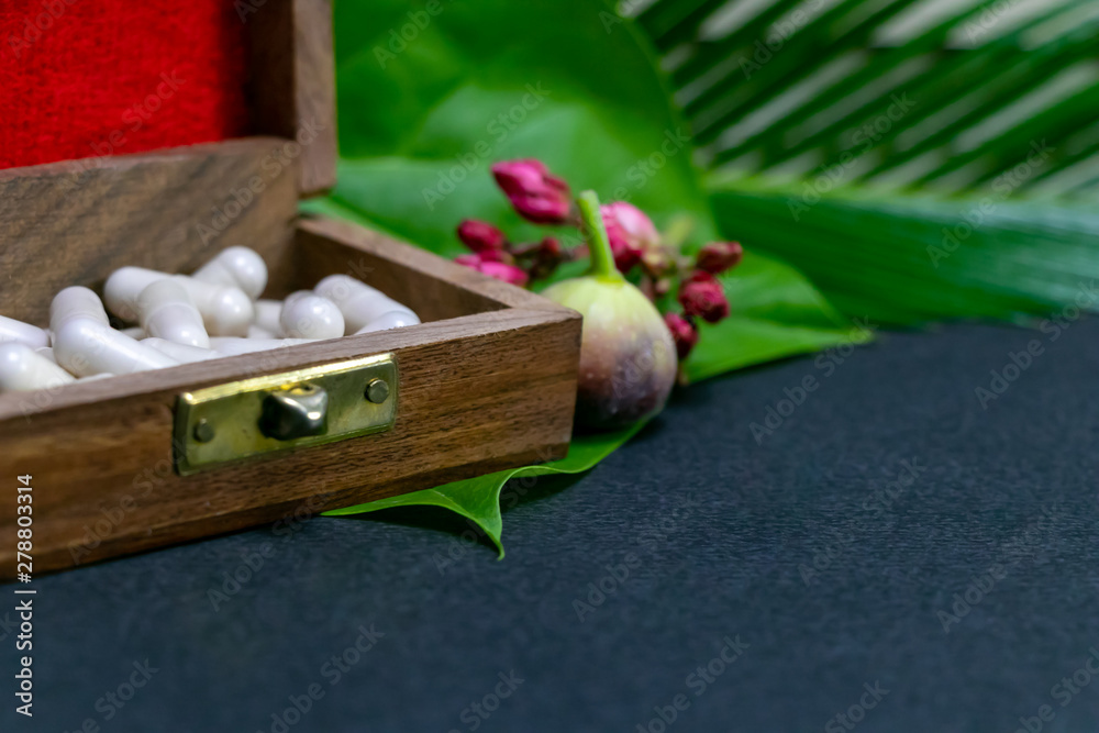 Fototapeta premium Herbal medicine capsules in wooden old box with flower bud, wild fruit and green leaf on dark background