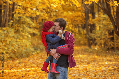 Father hugs and kisses his daughter in autumn day. The girl is holding a teddy bear.