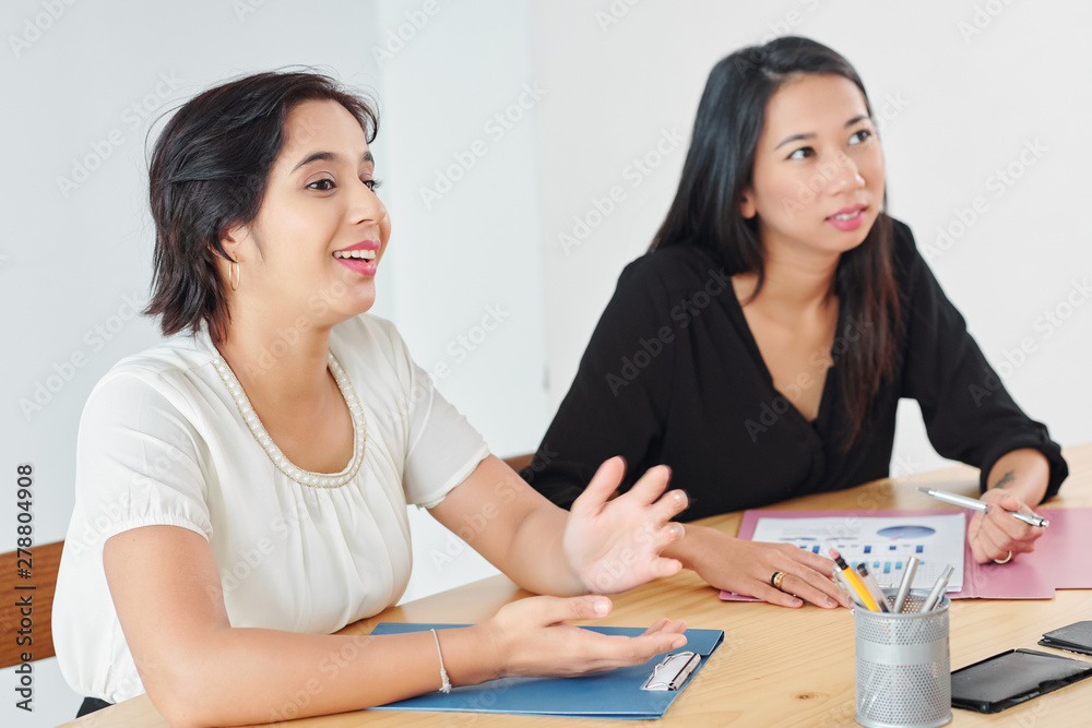 Two young colleagues sitting at the table communicating and discussing during business meeting at office Two young colleagues sitting at the table communicating and discussing during business meeting at office