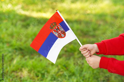 Hands of kid girl holding Serbia flag. Independence Day concept. Green grass background. © polack