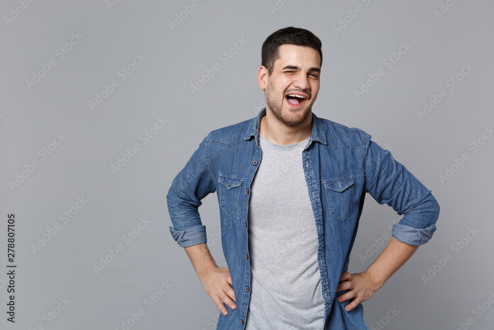 Handsome stylish unshaven young man in denim jeans shirt posing isolated on grey wall background studio portrait. People sincere emotions lifestyle concept. Mock up copy space. Looking camera smile. Handsome stylish unshaven young man in denim jeans shirt posing isolated on grey wall background studio portrait. People sincere emotions lifestyle concept. Mock up copy space. Looking camera smile.
