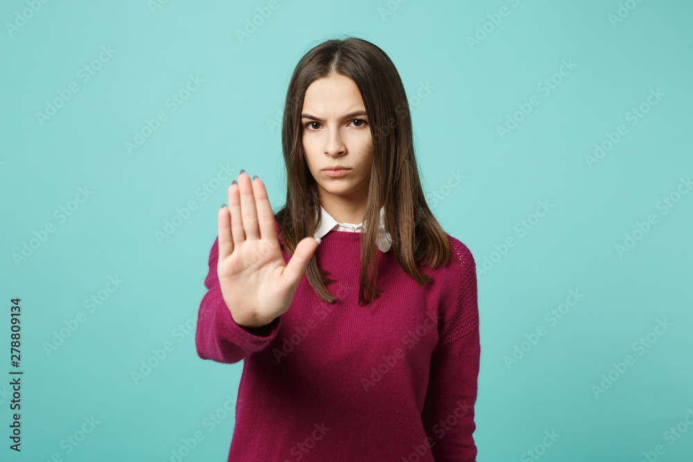 Fototapeta premium Young fun sad upset perplexed disturb brunette woman girl showing stop gesture with palm posing isolated on blue wall background studio portrait. People emotions lifestyle concept. Mock up copy space.