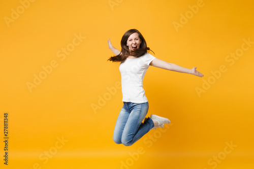 Portrait of funny screaming cheerful young woman in casual clothes jumping, spreading hand wall isolated on bright yellow orange background in studio. People lifestyle concept. Mock up copy space.