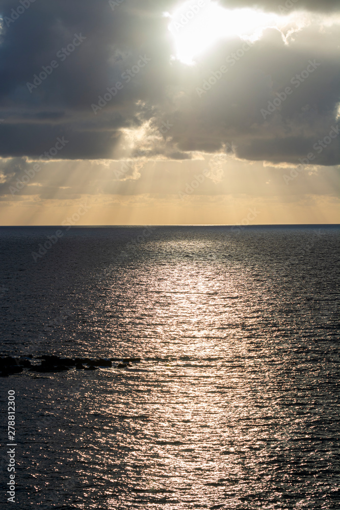 Dramatic sunset over sea water with gray clouds and sun lights