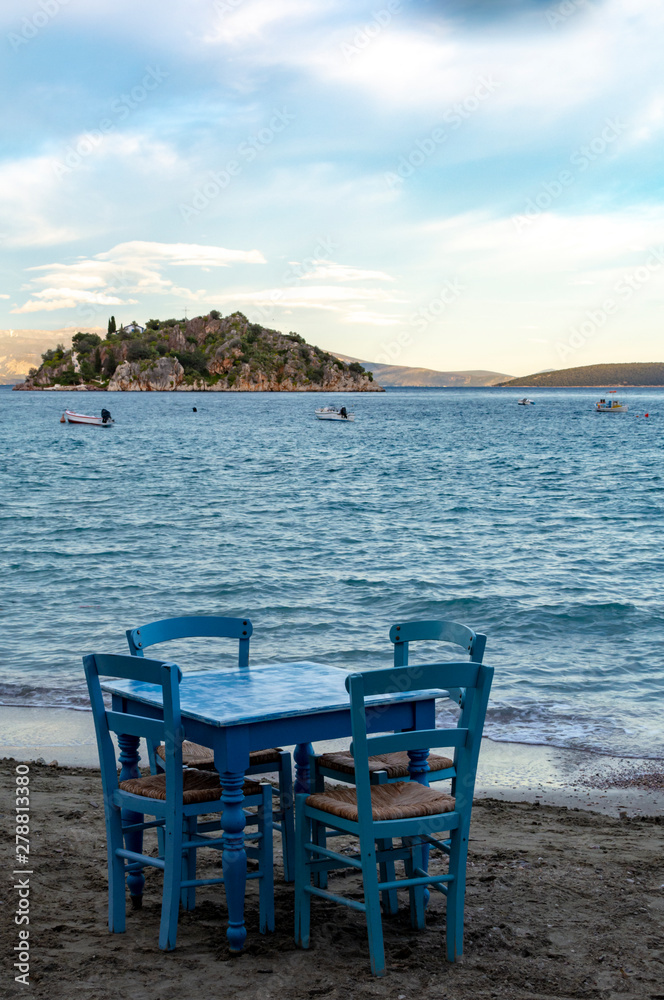 Traditional greek tavern with wooden tables on sandy beach near water waiting for tourists in Tolo, Peloponnese, Greece