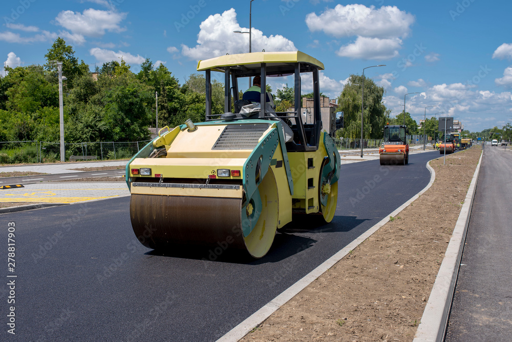 Obraz premium Road construction site. Asphalt roller compactor on site, compacting new asphalt pavement in urban modern city