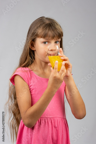 The girl drinks orange juice from a glass and looks at the frame