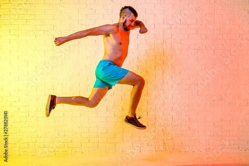 Young sporty man performs a jump on a yellow background.