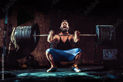 Muscular bearded tattoed fitness man doing deadlift a barbell over his head in modern fitness center. Functional training. Snatch exercise photo
