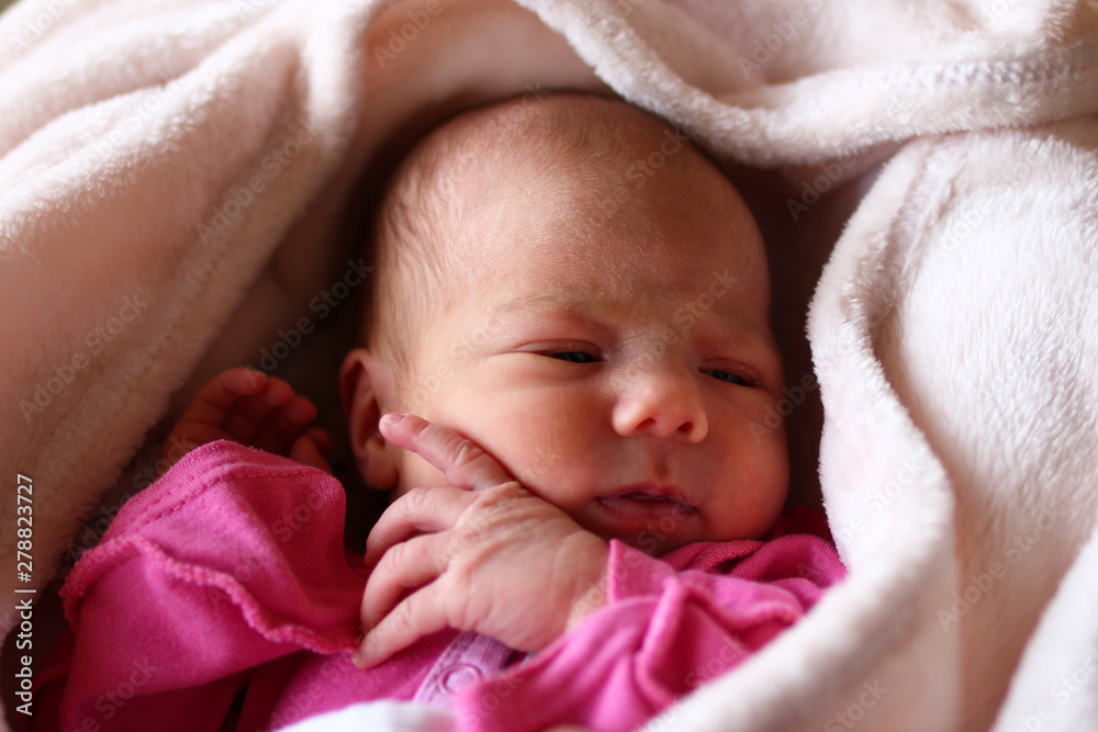 Cute sleeping newborn baby in pink baud on her bed under beige blanket. Cute sleeping newborn baby in pink baud on her bed under beige blanket.