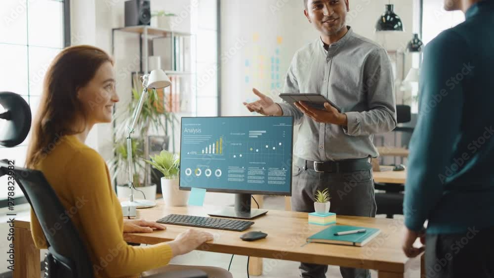 Three Economic Analytics Work on Desktop Computer, They Discuss Statistics, Graphs and Data, Use Touch Screen Digital Tablet. Modern Stylish Office with Diverse Team of Professionals Working