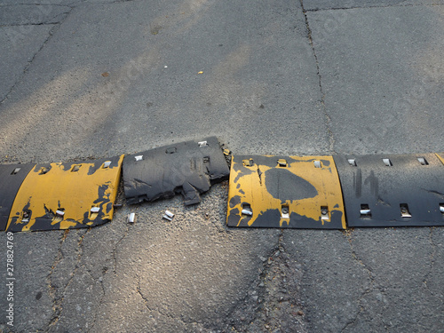 Broken after an accident yellow and black striped traffic safety speed bump on an asphalt road