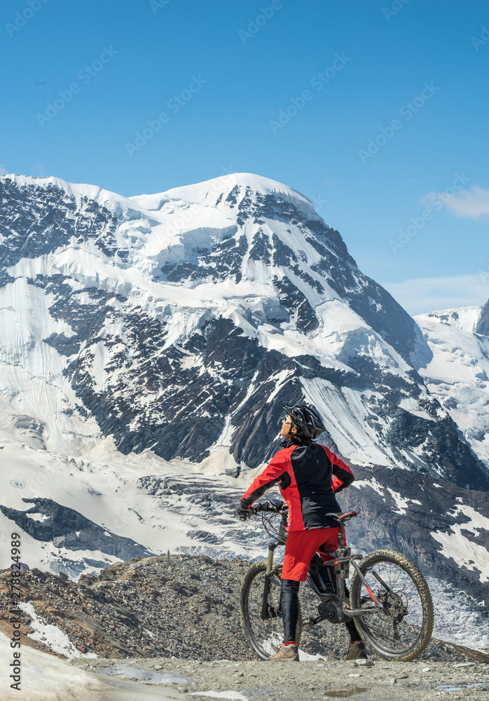 Fototapeta premium active senior woman, riding her electric mountainbikeon the Gornergrat in Zermatt, Wallis,Switzerland. In The background Gorner Glacier, Monte Rosa, Liskam am Breithorn