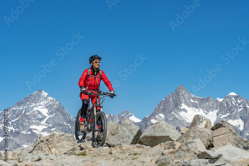 active senior woman, riding her electric mountainbikeon the Gornergrat in Zermatt, Wallis,Switzerland. In The background Weisshorn, Zinalrothorn and Obergabelhorn