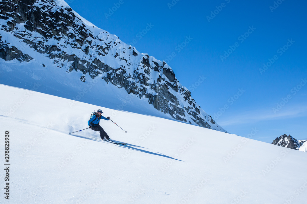 Skier on untouched powder slope under blue skies.
