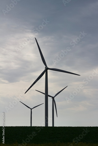 Silhouette of three giant wind turbines with a cloudy sky background