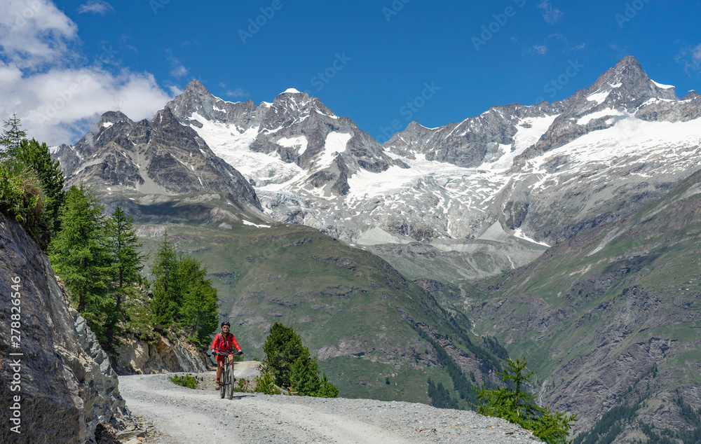 active senior woman, riding her electric mountain bike below the Gornergrat in Zermat, Canton Valais, Switzerland, in The background Zinalrothorn and Obergabelhorn