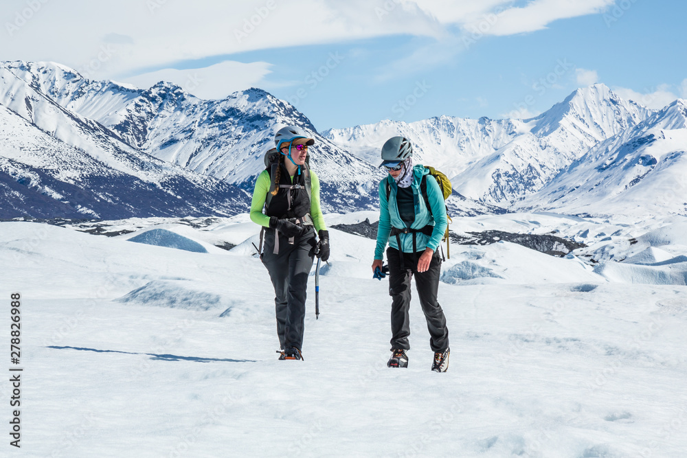 Two female glacier guides trekking through the Chugach Mountains on the Matanuska Glacier.