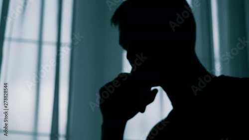 Anonymous blurred silhouette of a man talking on a cell phone in a dark room, a criminal is extorting money