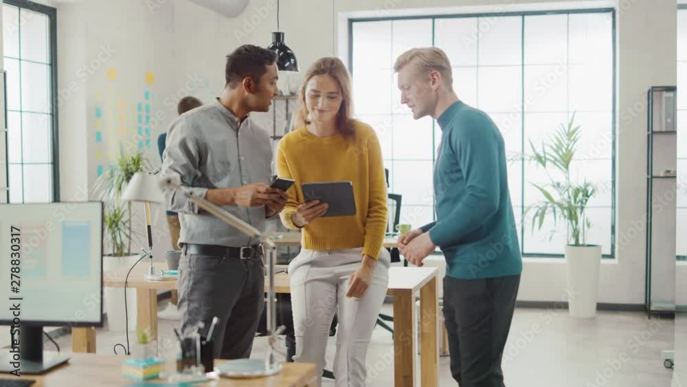 In the Office: Three Diverse Start-up Entrepreneurs Have Meeting and Discussion about the Project. Share Touch Screen Digital Tablet and Smartphone Screens.Young Professionals Smile and Joke Around