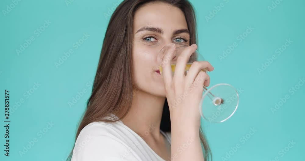 Beautiful girl drinks cold water with a yellow lemon. lemonade in a wine glass. Summer drink. Slow motion. Turquoise background. Beautiful girl drinks cold water with a yellow lemon. lemonade in a wine glass. Summer drink. Slow motion. Turquoise background.