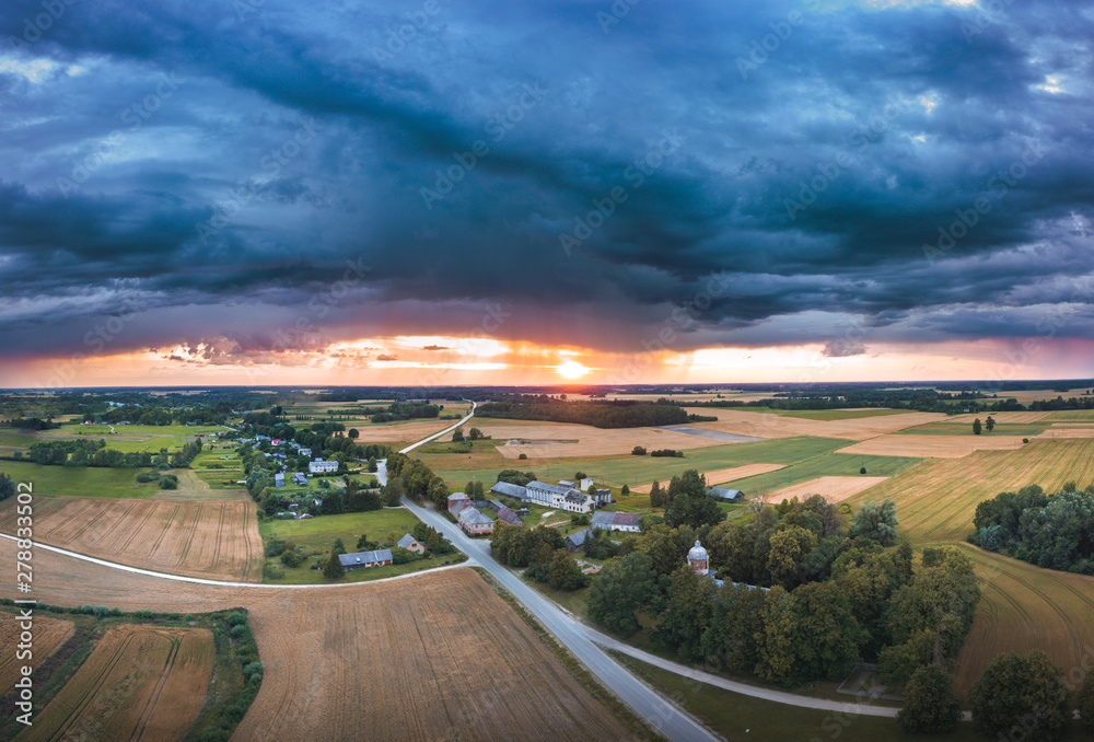 Aerial view on impressive thunderstorm over a countryside at sunset. Dark storm clouds covering the rural landscape. Intense rain shower in distance. 