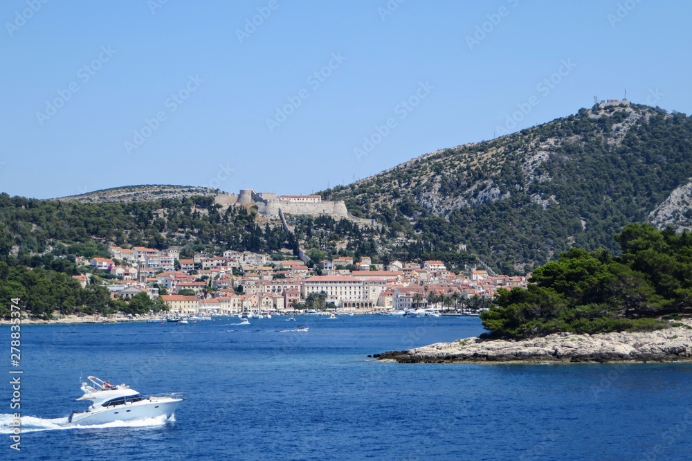 A faraway view from the ferry of the town of Hvar, on Hvar Island, Croatia.  It is a beautiful sunny summer day and the adriatic sea is calm.  Another boat is passing by the ferry.