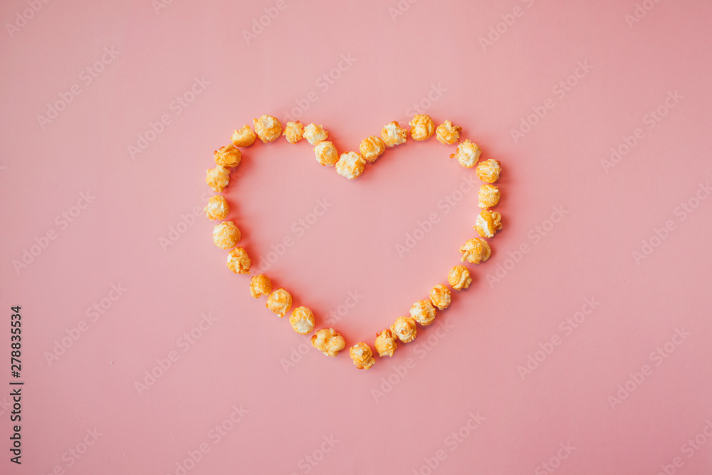 Love movies, concept on a pink background. Popcorn scattered on pink background heart shaped