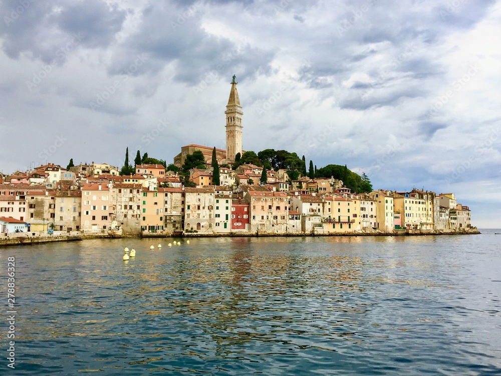 A view from the ocean facing the old town of Rovinj, Croatia.  Old colourful buildings and the clock tower dominate the skyline facing the beautiful adriatic sea.
