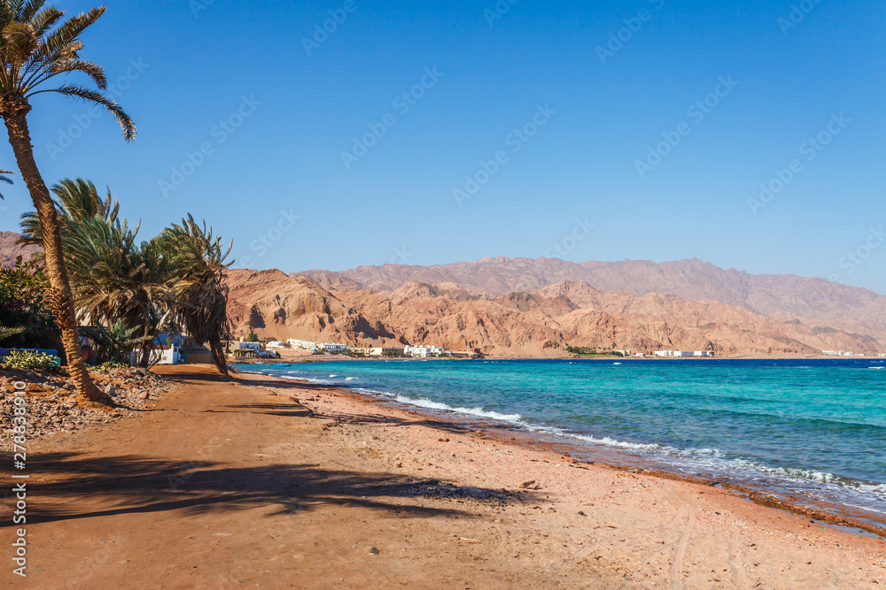 Sunny resort beach at the coast shore of Red Sea in Dahab, Sinai, Egypt, Asia in summer hot. Famous tourist destination near of Sharm el Sheikh. Bright sunny light Sunny resort beach at the coast shore of Red Sea in Dahab, Sinai, Egypt, Asia in summer hot. Famous tourist destination near of Sharm el Sheikh. Bright sunny light