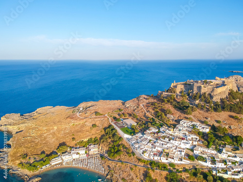 Aerial birds eye view drone photo of village Lindos, Rhodes island, Dodecanese, Greece. Sunset panorama with castle, Mediterranean sea coast. Famous tourist destination in South Europe.