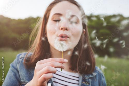 Portrait of teenage girl blowing dandelion photo