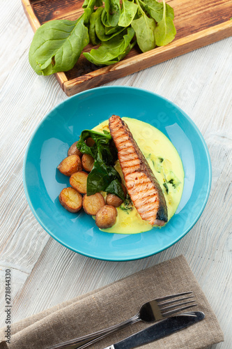 Top view of a grilled salmon steak with baked baby potatoes, spinach and coconut milk gravy served on a wooden table