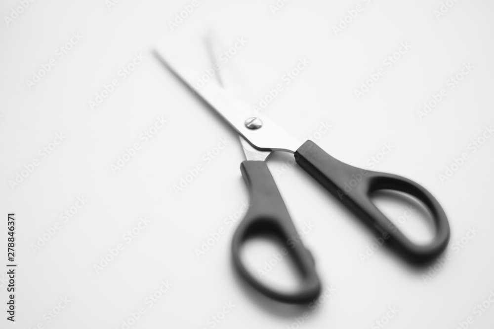 Open scissors with a black handle lie on a white surface Open scissors with a black handle lie on a white surface
