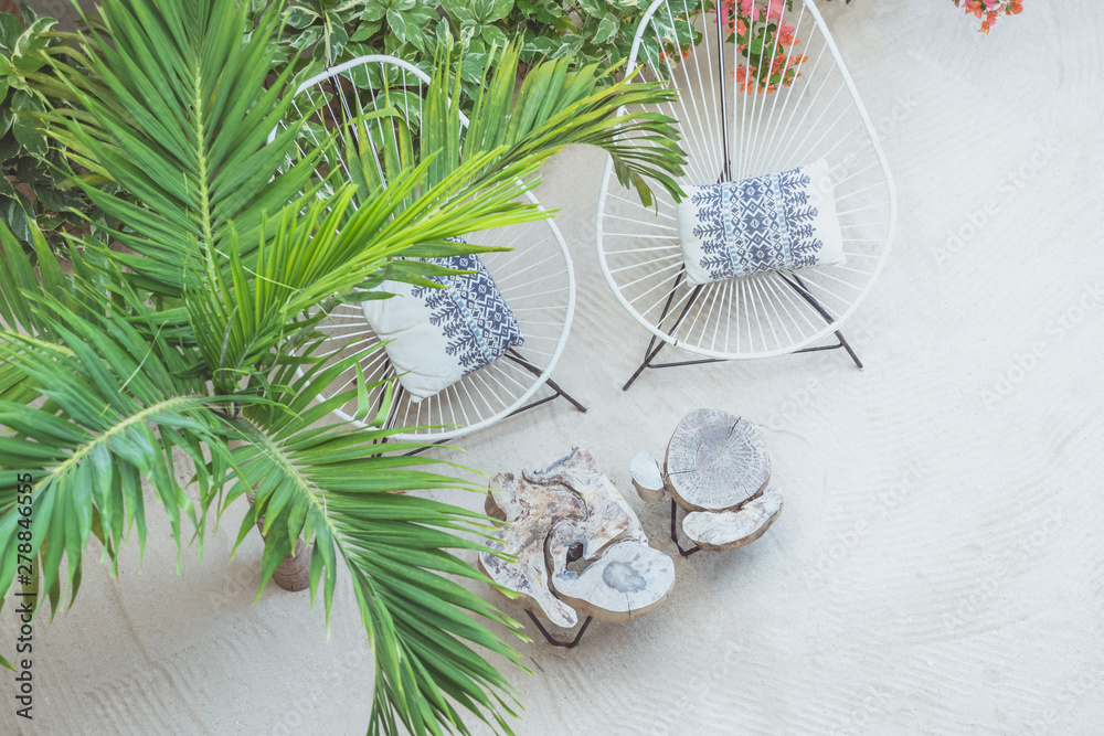 Outdoor chairs and wooden tables standing besides a palm tree on sandy beach Outdoor chairs and wooden tables standing besides a palm tree on sandy beach