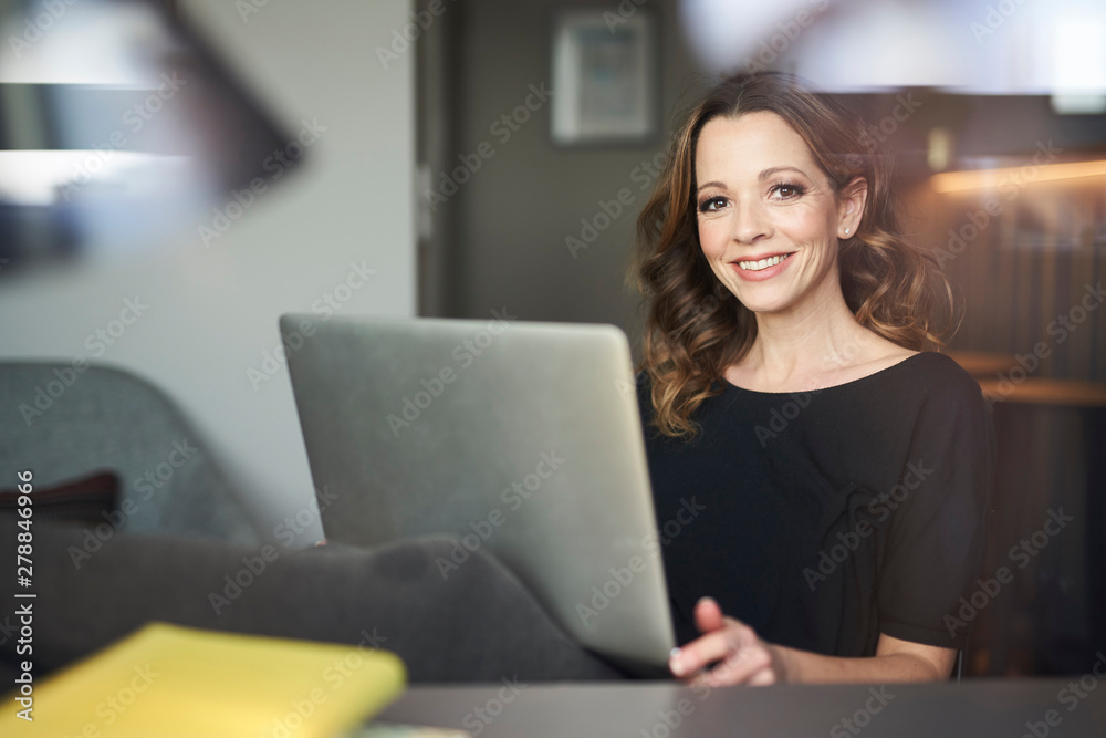 Portrait of smiling woman with laptop behind windowpane Portrait of smiling woman with laptop behind windowpane