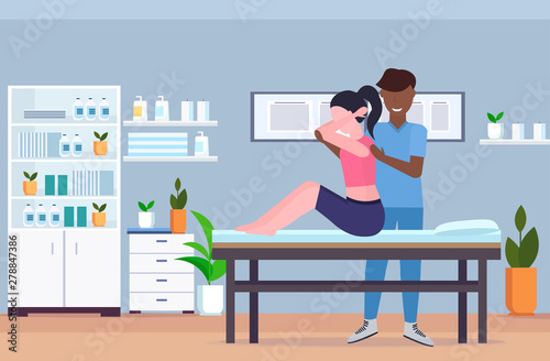 woman sitting on massage table african american masseur doing healing treatment massaging injured patient manual physical therapy rehabilitation concept hospital office interior horizontal