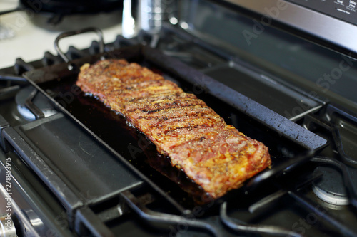 Rack of dry rub pork ribs baked on a carbon steel tray, resting on the stove top.
