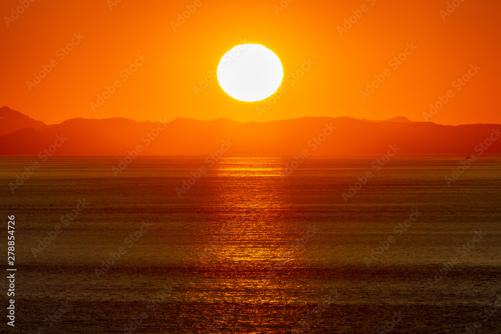 Beautiful golden sunset/sunrise over the sea behind mountains in background. Light reflection on the water as the sun sets/rises. Harmony and beauty in nature. Scenic peaceful ocean view.