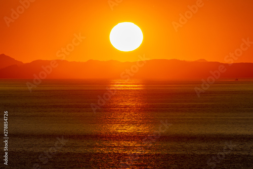 Beautiful golden sunset/sunrise over the sea behind mountains in background. Light reflection on the water as the sun sets/rises. Harmony and beauty in nature. Scenic peaceful ocean view. © Debbie Ann Powell