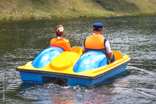 A young couple - a Russian girl and a guy dressed in a traditional national costume and a Tatar cap ride on a catamaran pleasure boat with a pedal on the pond of a city park