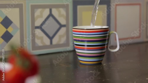 DOLLY SHOT WITH TOMATOES IN THE FOREGROUND AND SOMEONE POURING HOT WATER FROM A BIGHT GREEN ELECTRIC KETTLE photo